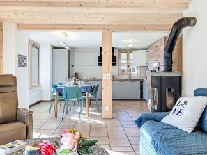 Une cuisine moderne dotée d’une cuisinière intégrée, un coin repas avec une table et des chaises, et un salon avec un canapé et un coussin décoratif.