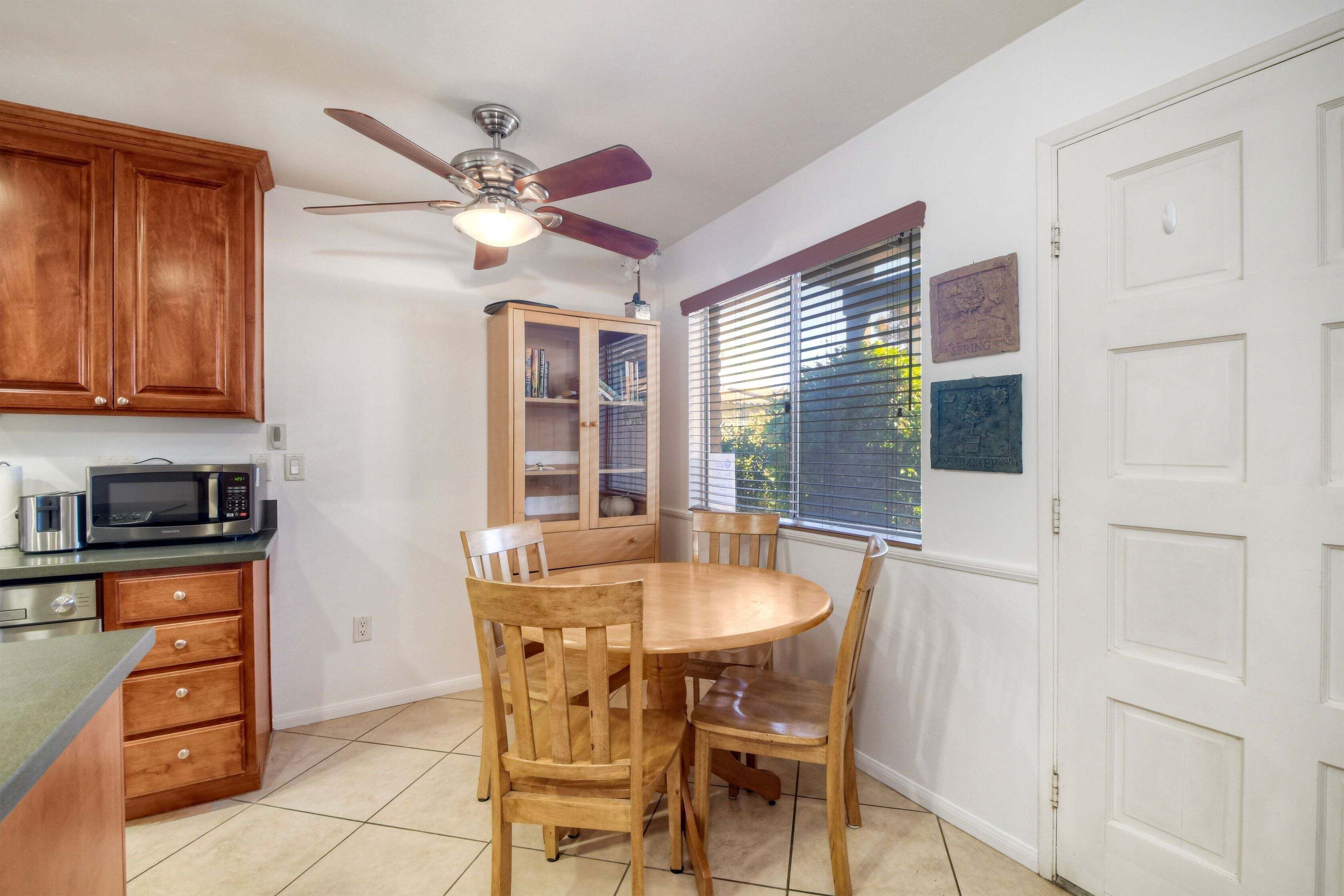 Une cuisine avec des meubles de rangement en bois, un four à micro-ondes, un ventilateur de plafond et une table à manger avec des chaises.