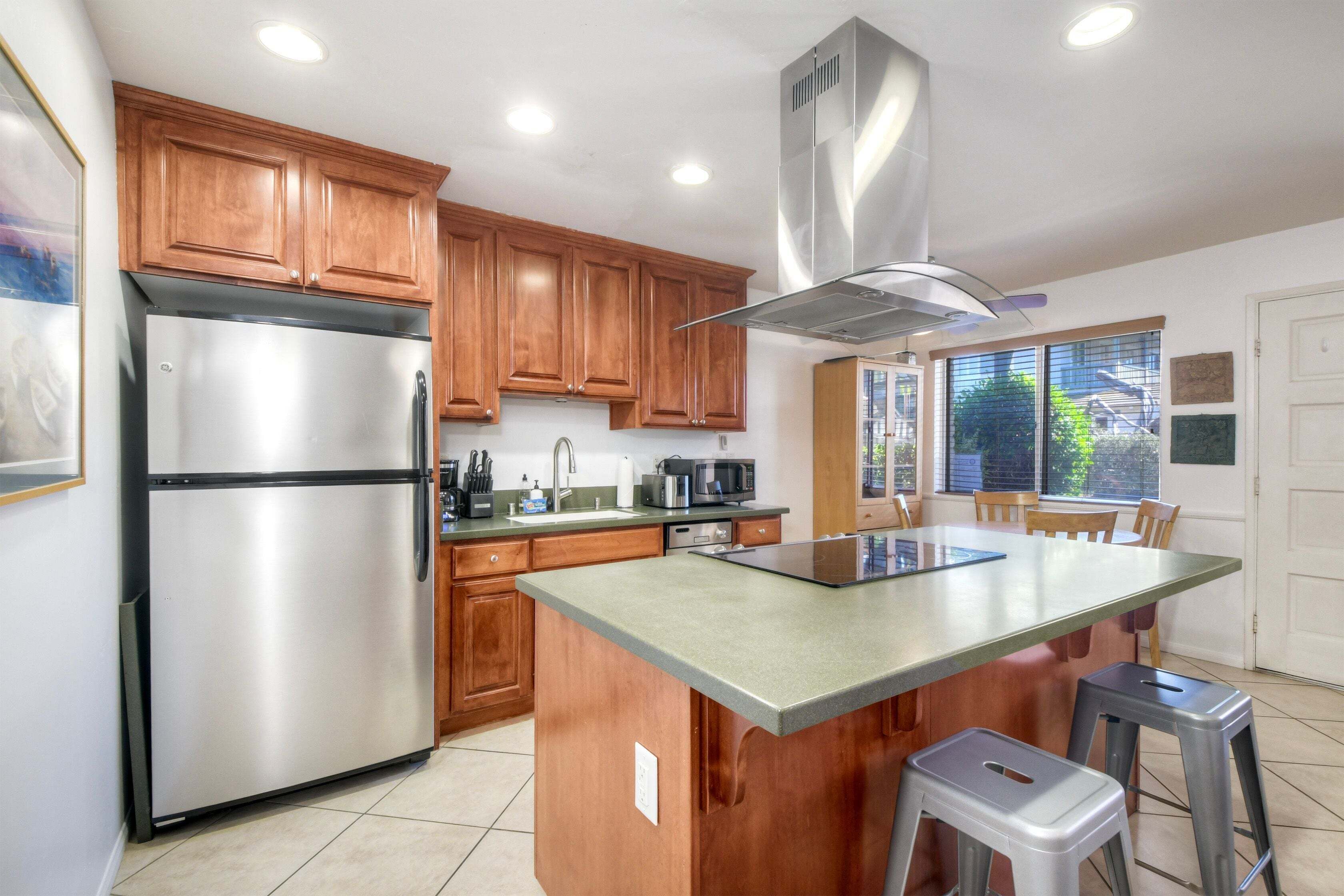 A kitchen with wooden cabinets, a stainless steel refrigerator, a microwave, and a large island with stools.
