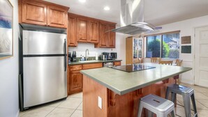 A kitchen with wooden cabinets, a stainless steel refrigerator, a microwave, and a large island with stools. - 90 Walk Score l Private Patio | Steps to Beach & Dining | Parking (Carlsbad)