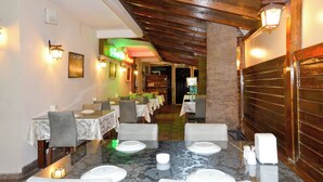 A restaurant with tables set for dining, wooden beams on the ceiling, and wall-mounted lights. - Green Palm Hotel (Marmaris)