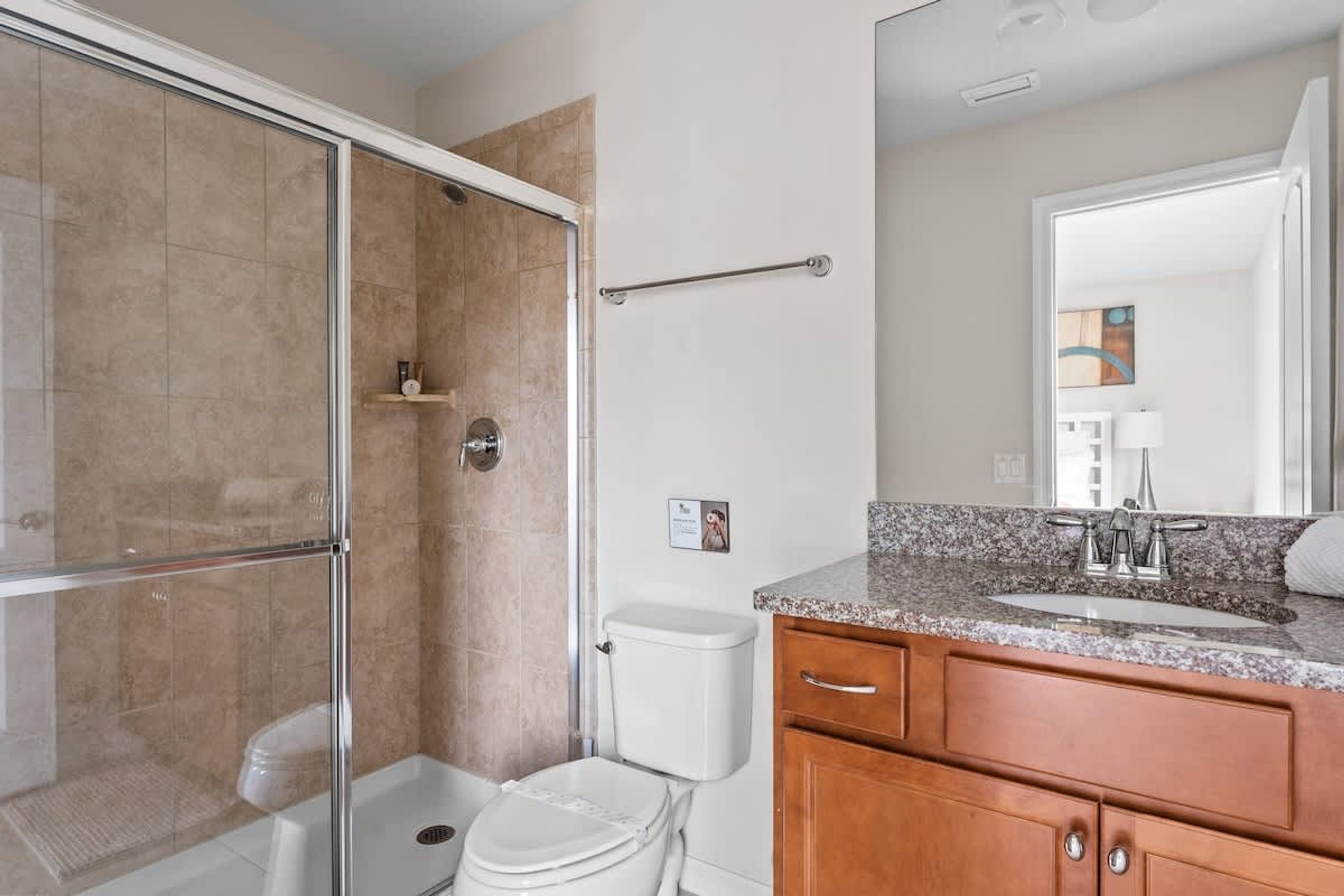 Un bagno moderno con box doccia in vetro, un water, un lavabo con piano in granito e mobili in legno.