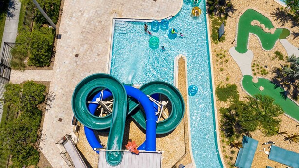 An aerial view of a swimming pool area with a water slide, a small pool, and surrounding landscaping. - Cozy & Stylish 2BR Condo, Prime Storey Lake Spot (Kissimmee)