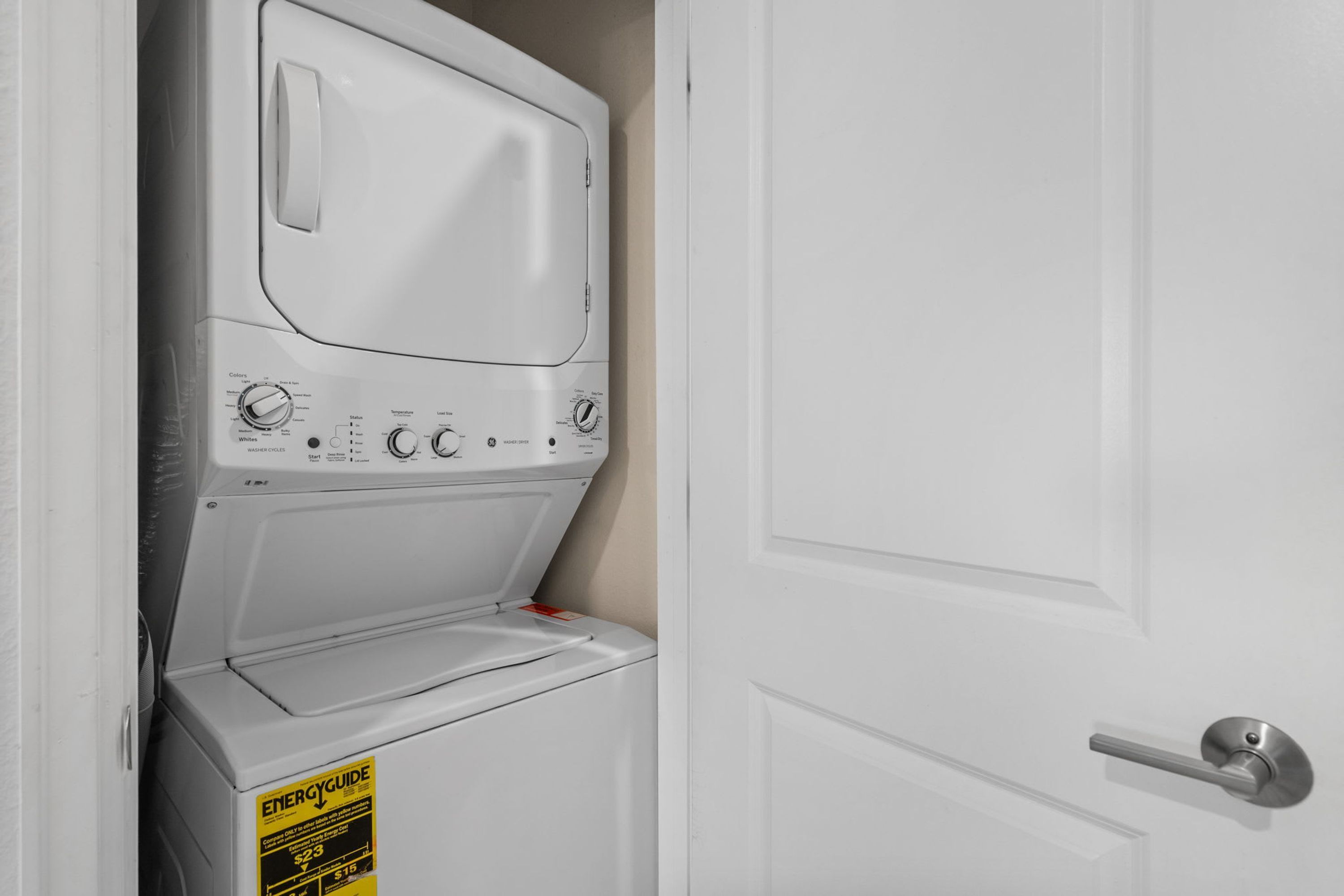 Une machine à laver blanche se trouve dans une buanderie, avec une porte et une poignée en métal.