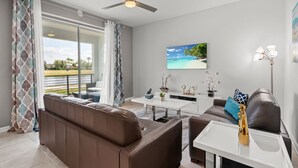 A modern living room with a brown leather sofa, a white coffee table, and a ceiling fan. - Cozy & Stylish 2BR Condo, Prime Storey Lake Spot (Kissimmee)