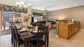A spacious dining area with a large wooden table, multiple chairs, and a chandelier. There is a kitchen area with a granite countertop and wooden cabinets. - Lovely House for 10 People at Paradise (Four Corners)