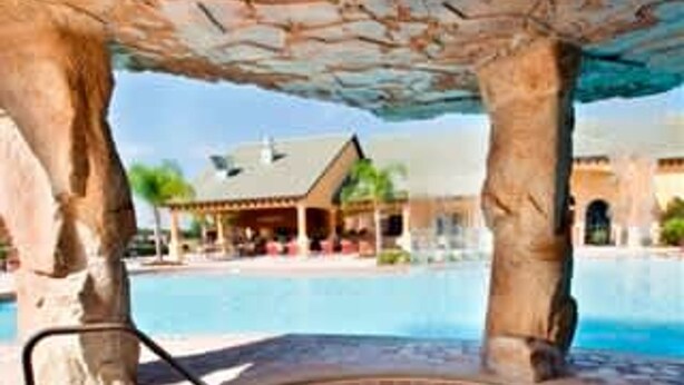 A circular hot tub with a clear blue pool in the background, surrounded by stone pillars and a building with a roof. - Lovely House for 10 People at Paradise (Four Corners)