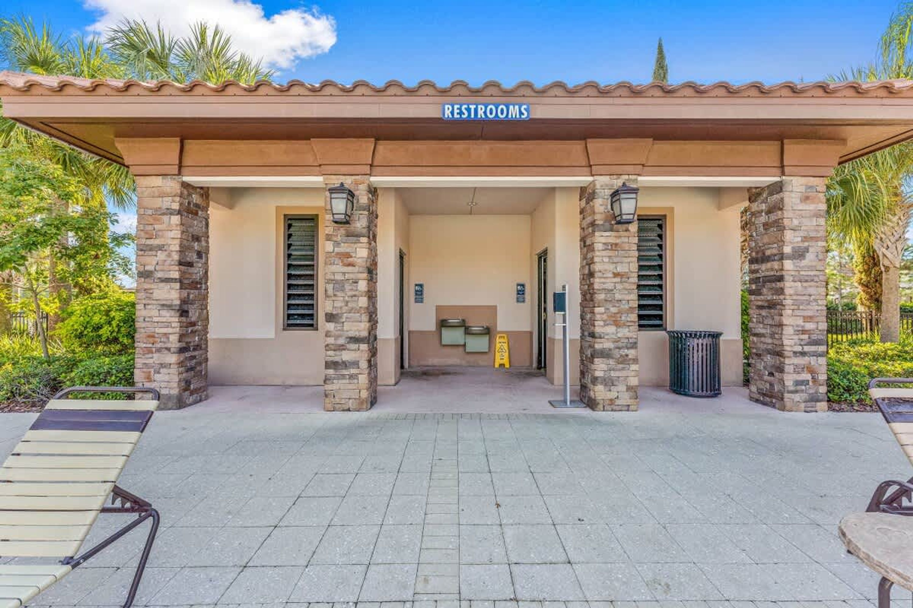 A building with a sign labeled "RESTROOMS" at the entrance, stone pillars, and a paved walkway leading to the entrance.
