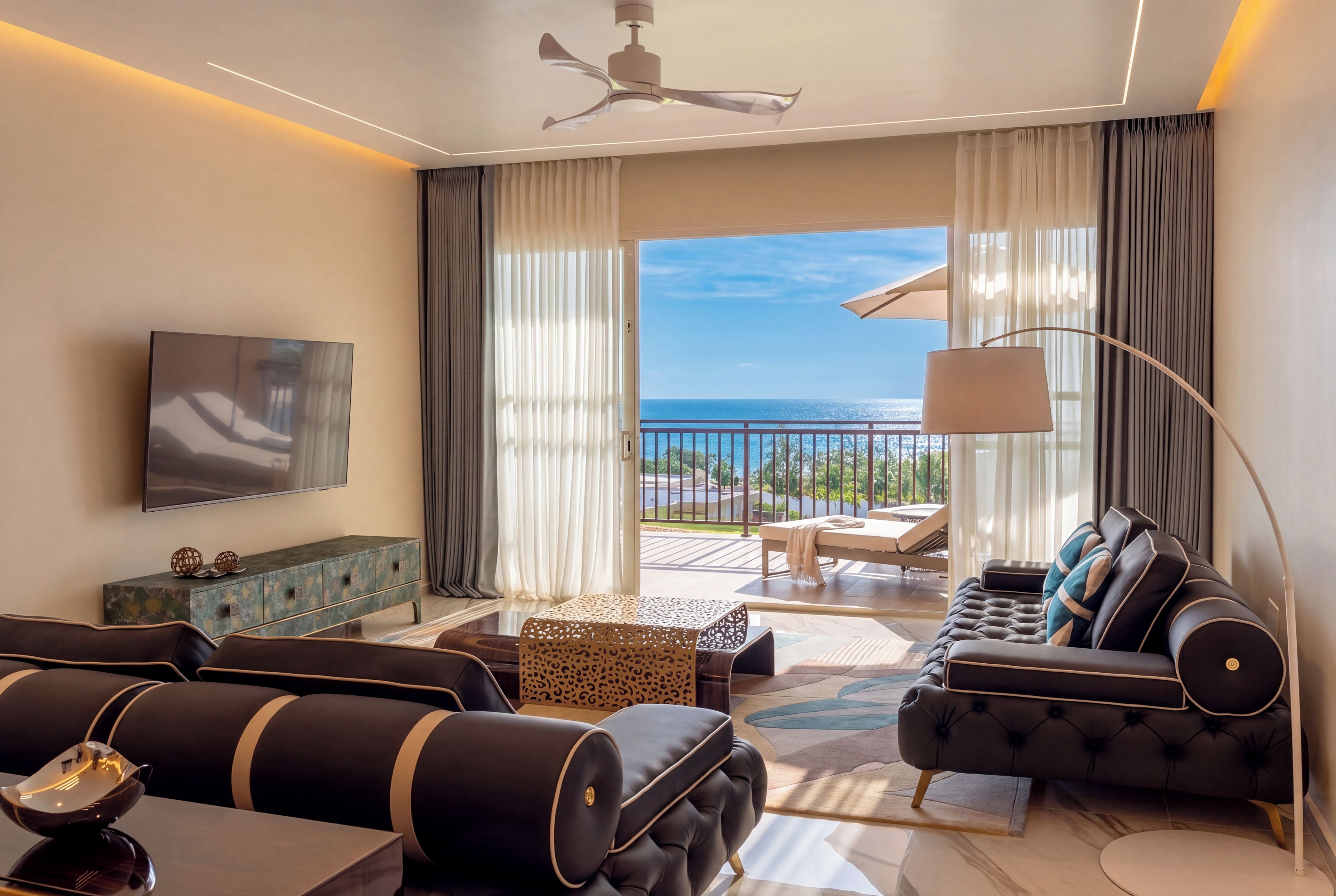 A modern hotel room with a balcony, a flat-screen TV, a sofa, and a dining area.