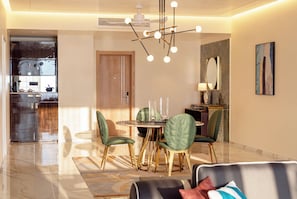 Un espace de salle à manger moderne avec une table ronde, des chaises recouvertes d’un tissu vert et un lustre.