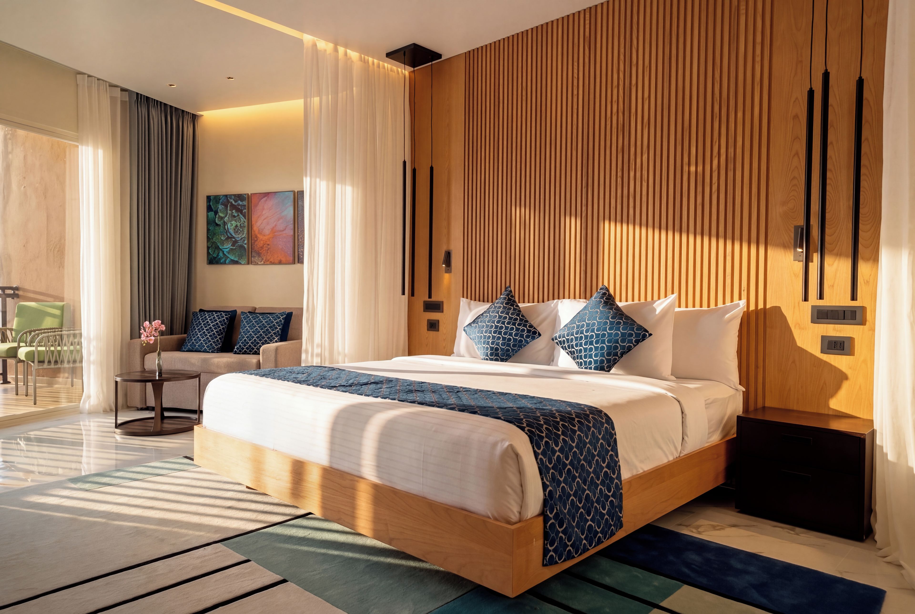 A modern hotel room with a large bed, a wooden headboard, and a view of the outdoors.