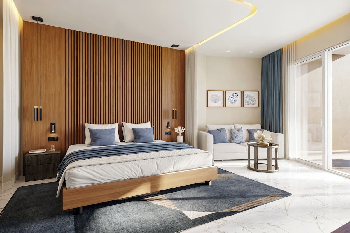 Un dormitorio moderno con cabecera de madera, cama grande, mesita de noche, sofá, una pequeña mesita auxiliar y un ventanal amplio.