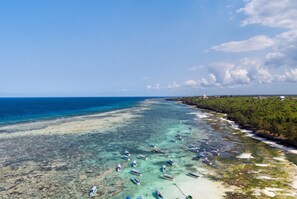 An aerial view of a beach with clear turquoise waters, boats anchored along the shore, and a backdrop of lush greenery. - Iberostar Selection Zanzibar – All-Inclusive (Matemwe)