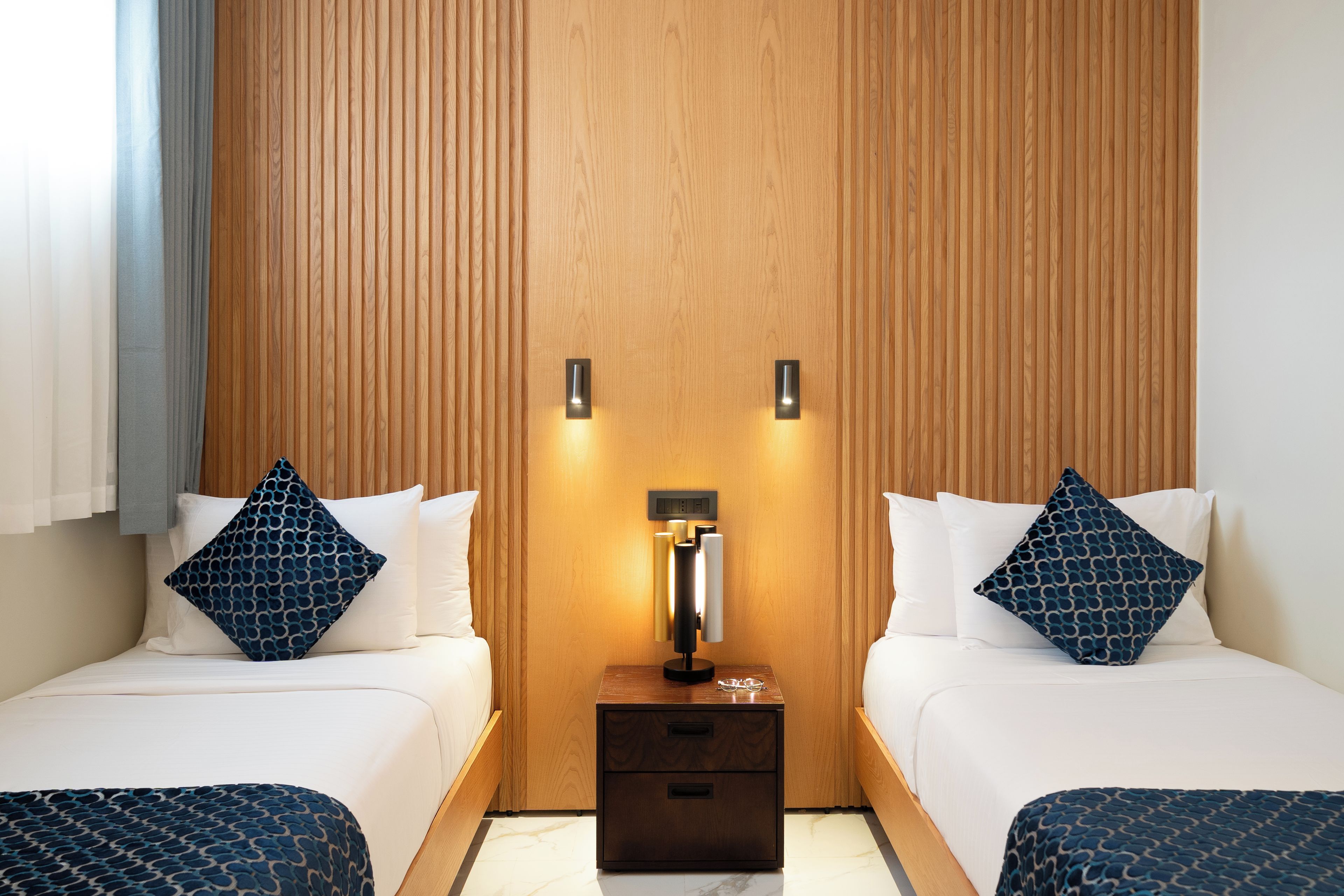Une chambre d’hôtel avec deux lits, une table de chevet avec une lampe et un mur recouvert de panneaux de bois.