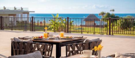 Una mesa de comedor con alimentos para el desayuno y vista al océano.