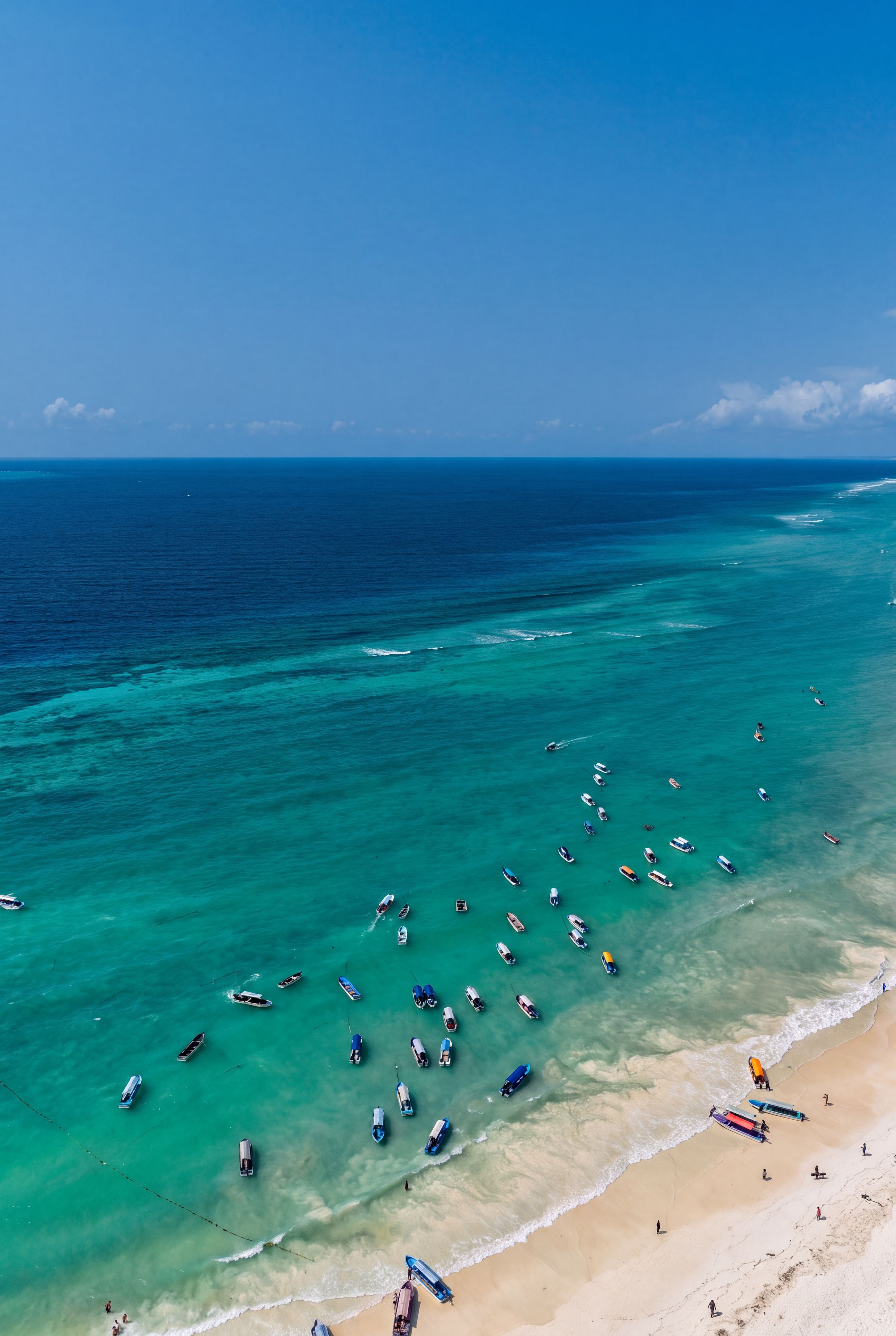 A beach with numerous boats anchored in the water and people on the sand.