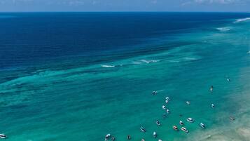 A beach with numerous boats anchored in the water and people on the sand.