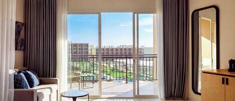 A hotel room with a bed, a sofa, a small table, a balcony with a view of the city, and a large mirror.