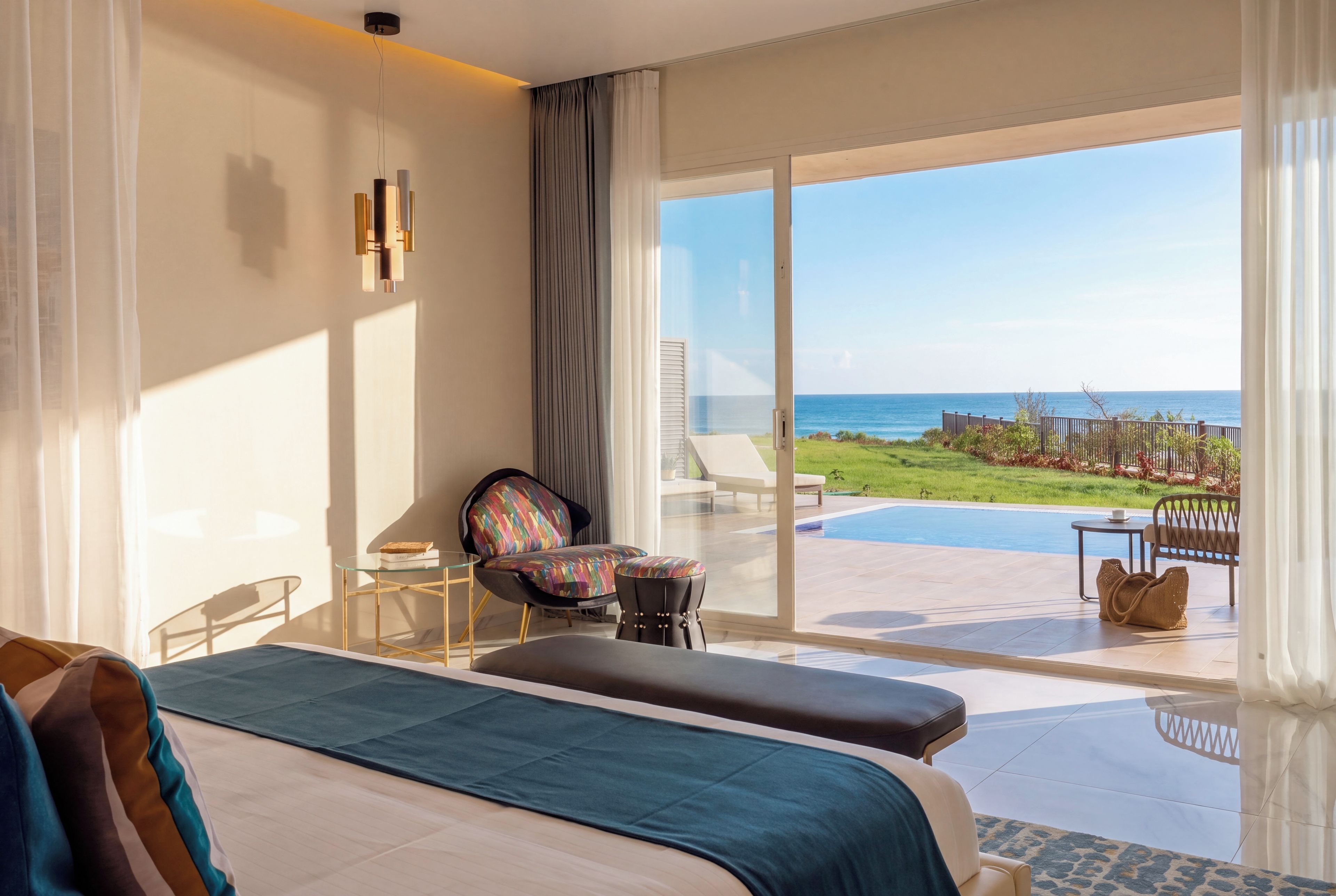 A hotel room with a large bed, a seating area with a view of the ocean, and a balcony with a pool.