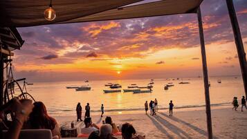 A beach scene with a sunset, boats, and people on the sand.