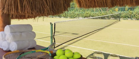 A tennis court with a net, a basket of tennis balls, and a rack of towels.