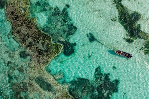 A boat on clear turquoise water with rocky formations. - Iberostar Selection Zanzibar – All-Inclusive (Matemwe)