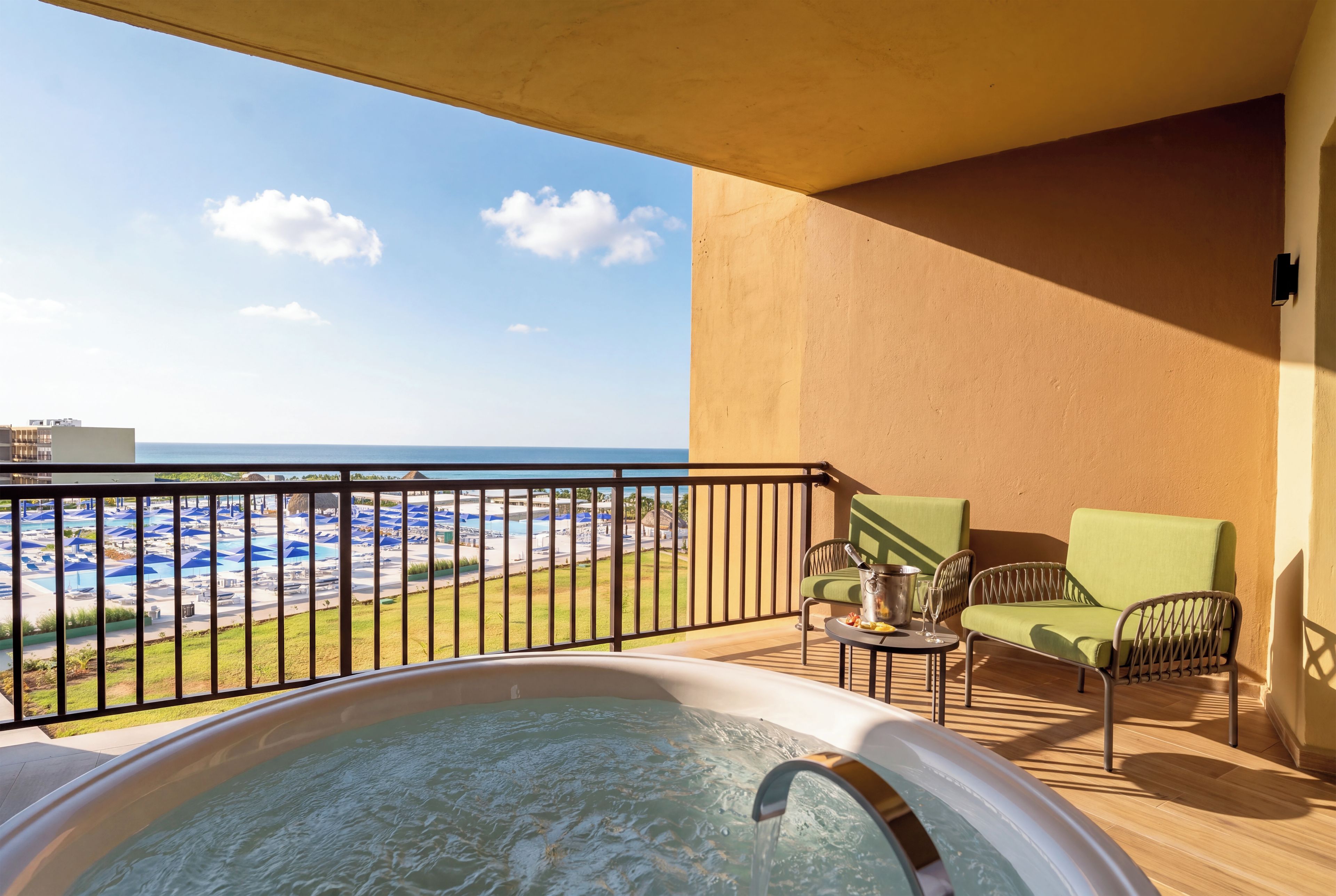 Un balcón con jacuzzi, mobiliario exterior y vistas a una piscina y una playa.