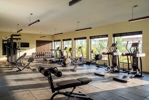A well-lit gym with various exercise equipment, large windows, and a tiled floor.