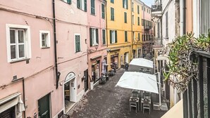 Eine enge Straße mit Gebäuden an beiden Seiten, mit einem Café mit Außenbestuhlung und einigen Personen.