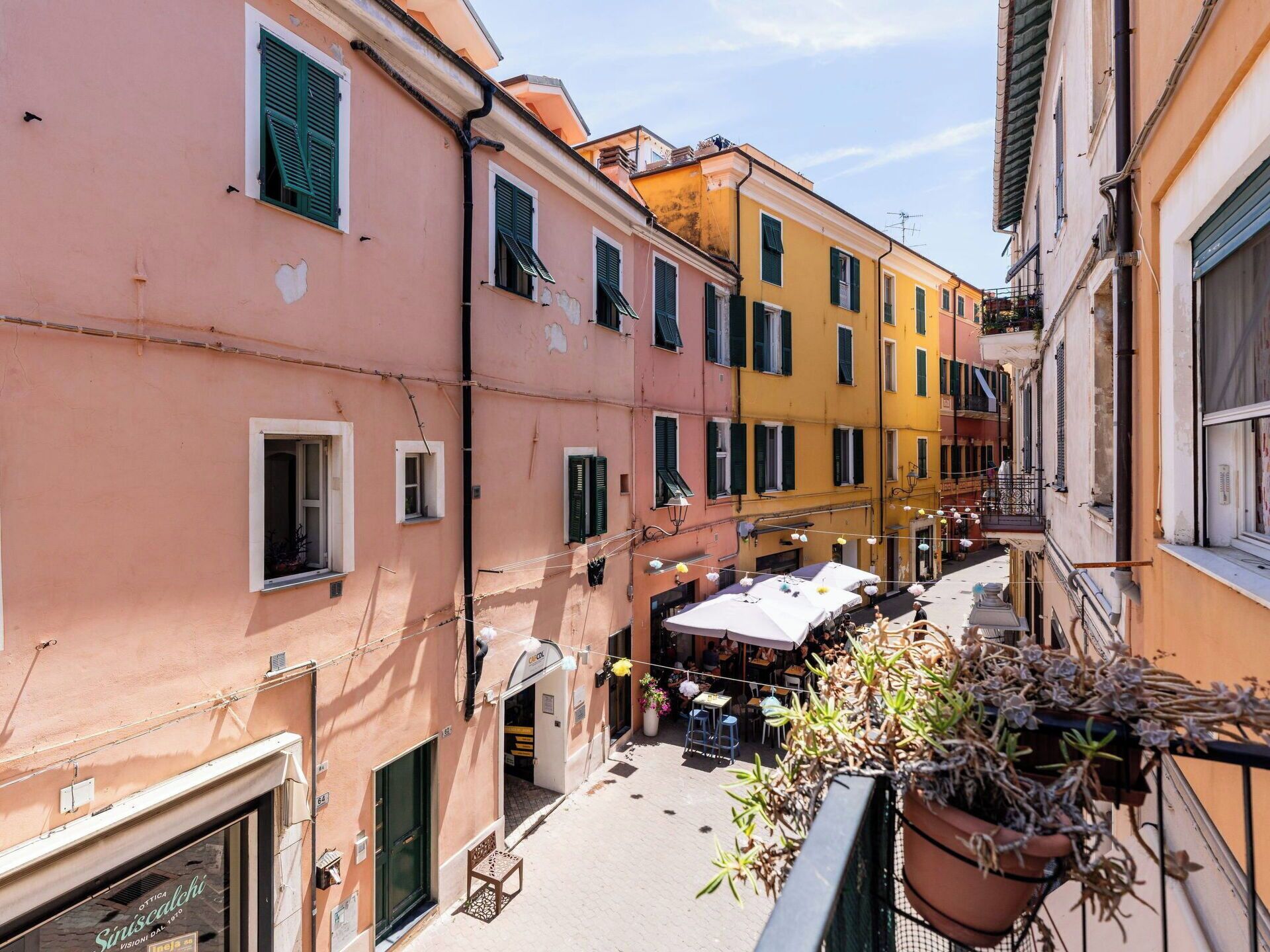 A narrow street with colorful buildings, outdoor seating, and a potted plant.