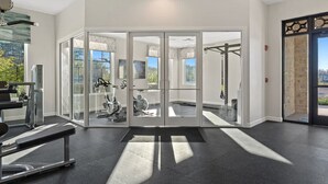A modern gym with glass doors, exercise equipment, and a view of the outdoors. - Beautiful Decor 2BR Apartment Near Disney (Kissimmee)