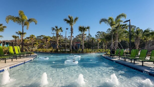 A pool with water jets, surrounded by palm trees and green lounge chairs. - Beautiful Decor 2BR Apartment Near Disney (Kissimmee)