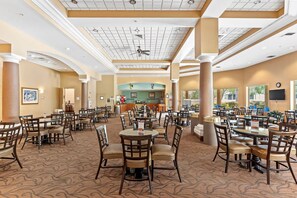 Un vaste espace dédié à la salle à manger, avec de nombreuses tables et chaises, un bar central et de grandes fenêtres qui laissent entrer la lumière naturelle.