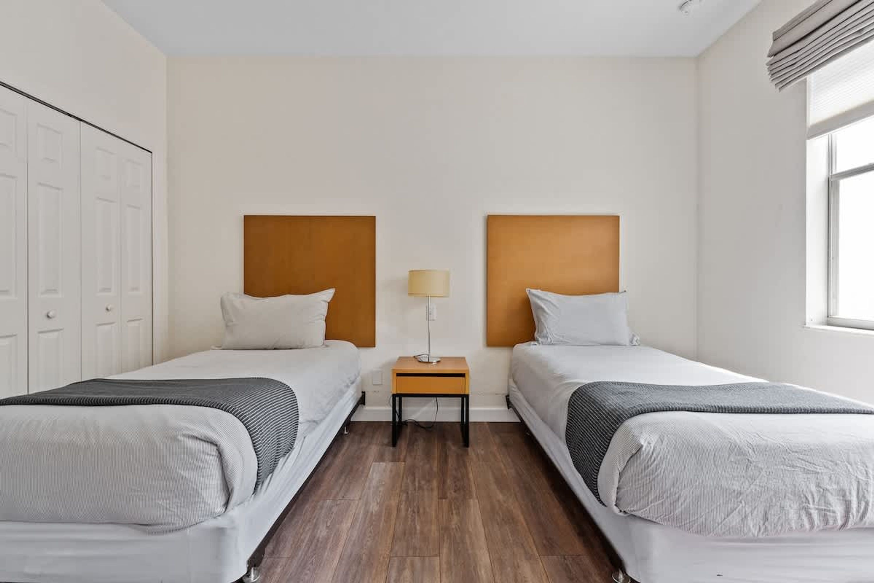 Una habitación de hotel con dos camas individuales, una mesita de noche con lámpara y un armario.