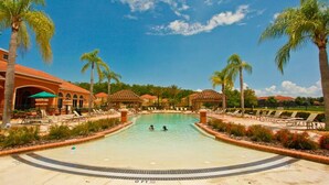 A swimming pool with lounge chairs and palm trees, surrounded by buildings with red roofs. - Amazing House at Bella Vida 5BR (Kissimmee)