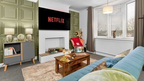 En stue med et fladskærms TV, pejs, sofa, sofabord og en bogreol.