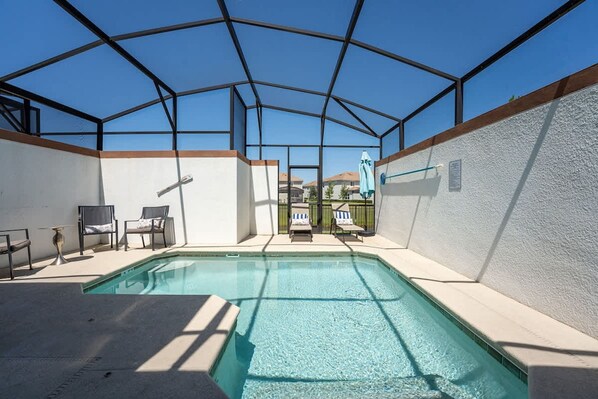 Una piscina interior con techo de vidrio, rodeada de sillas de descanso y vista a edificios al fondo.