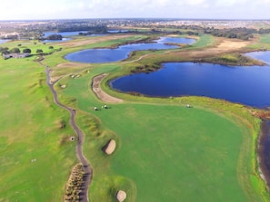 Luftaufnahme eines Golfplatzes mit mehreren Teichen, grünen Spielbahnen und Sandbunkern.