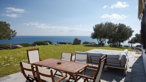Zona relax all'aperto con tavolo e sedie, con vista panoramica sul mare e sul paesaggio roccioso.