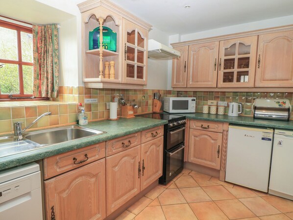A kitchen with wooden cabinets, a microwave, a toaster, and a dishwasher. - The Stables (Sturminster Newton)