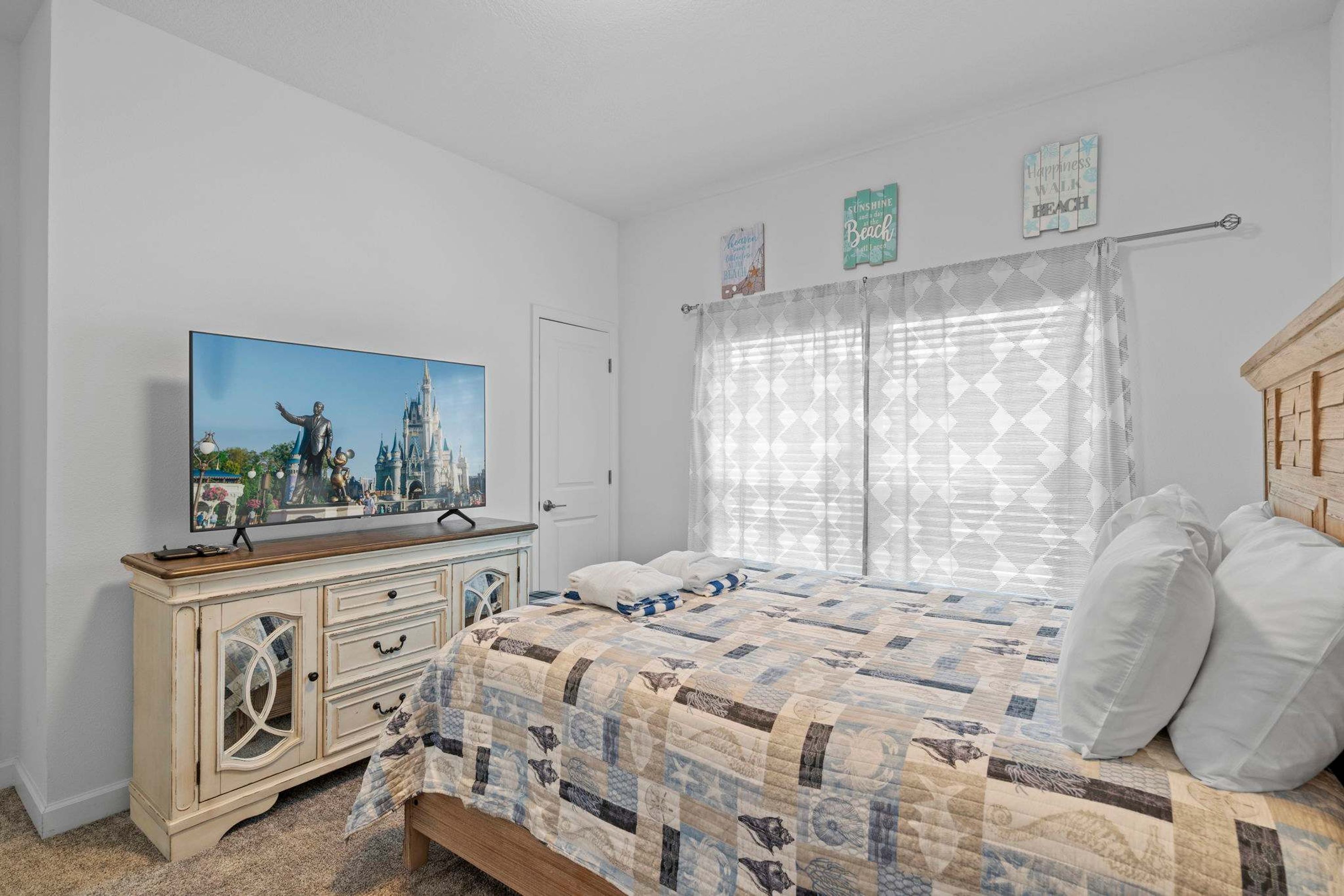 Un dormitorio con cama, cómoda, televisión y ventana con cortinas.