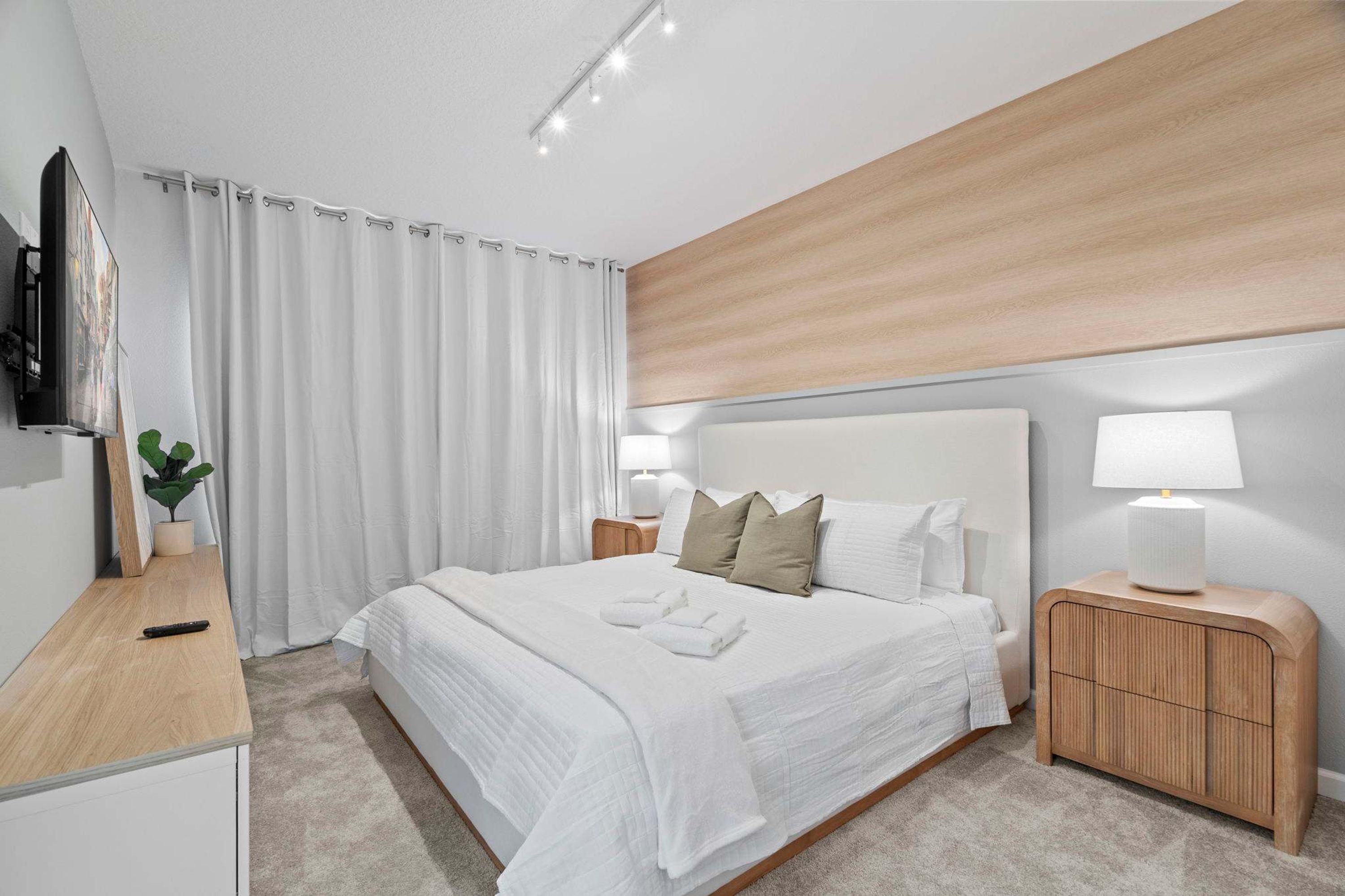 Een moderne hotelkamer met een groot bed, twee nachtkastjes met lampen, een flatscreen televisie en een groot raam met gordijnen.