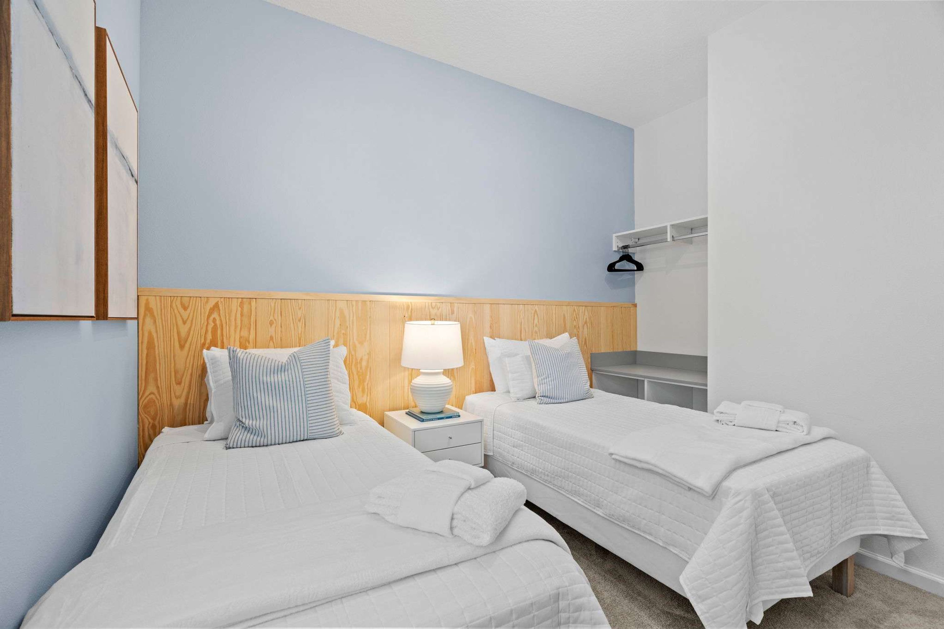 A hotel room with two beds, a wooden headboard, a nightstand with a lamp, and a white wall.