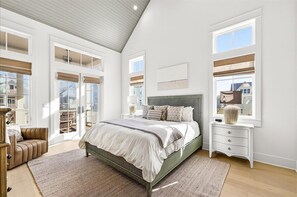 Ein Schlafzimmer mit Bett, Nachttisch, Sessel und großen Fenstern.