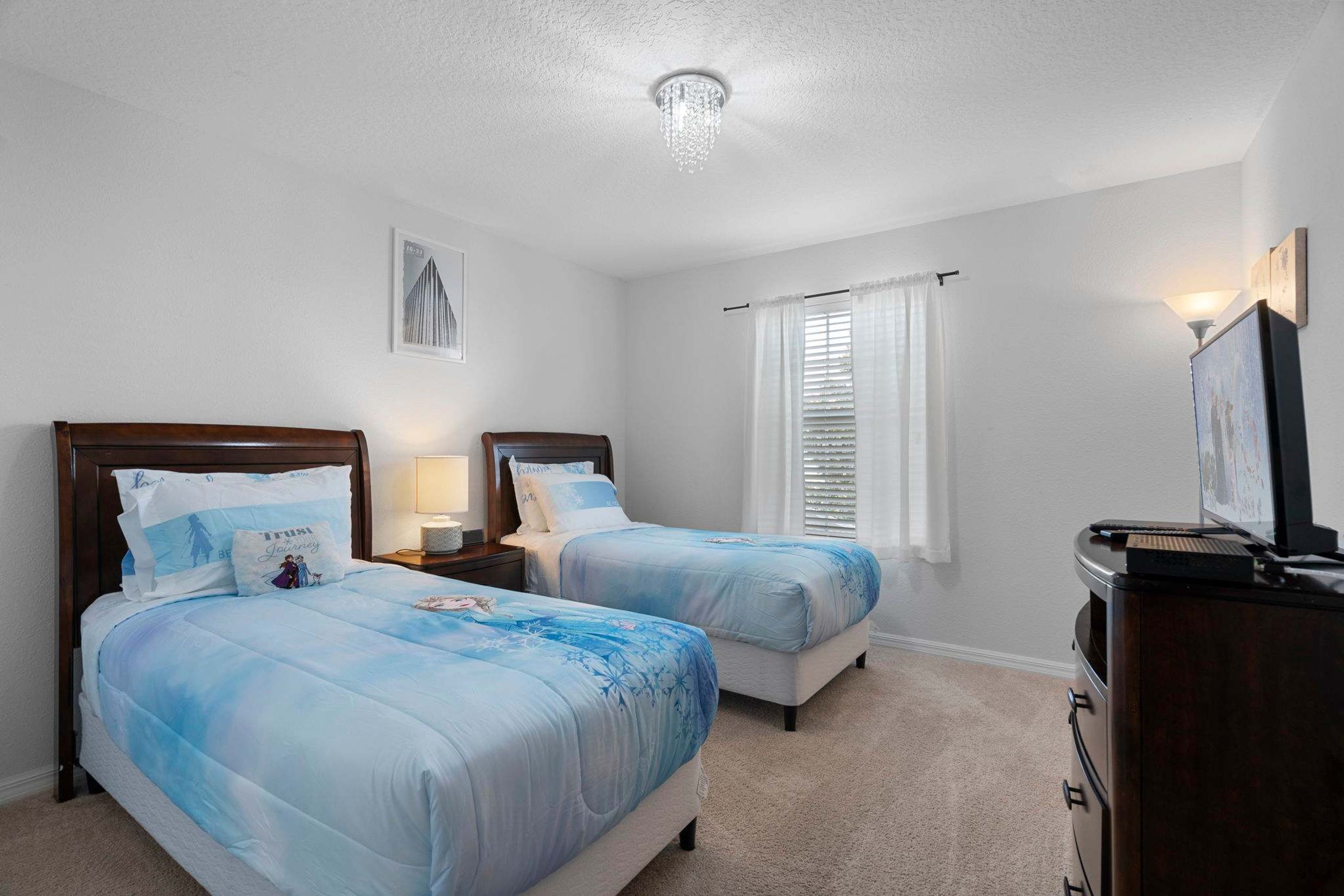 Une chambre avec deux lits, une commode, une table de chevet, un lustre et une fenêtre avec des rideaux.