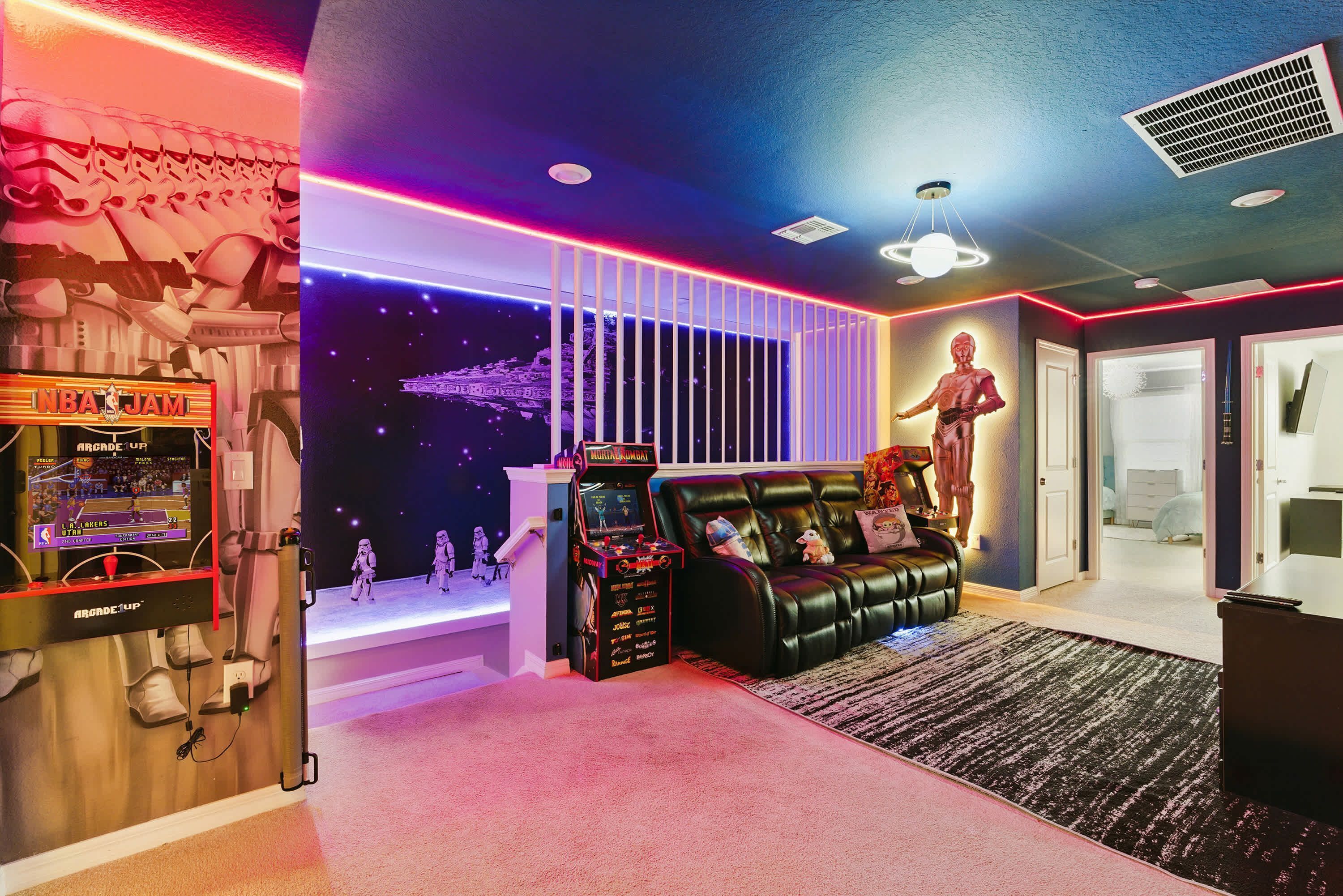A room with a gaming arcade, a black leather couch, and a Star Wars-themed wall.