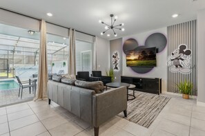 Un salon moderne avec un canapé gris, un téléviseur fixé au mur et une piscine visible à travers la porte vitrée.