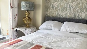 A hotel room with a large bed, a gold bust on a nightstand, a patterned wall, and a window with curtains.