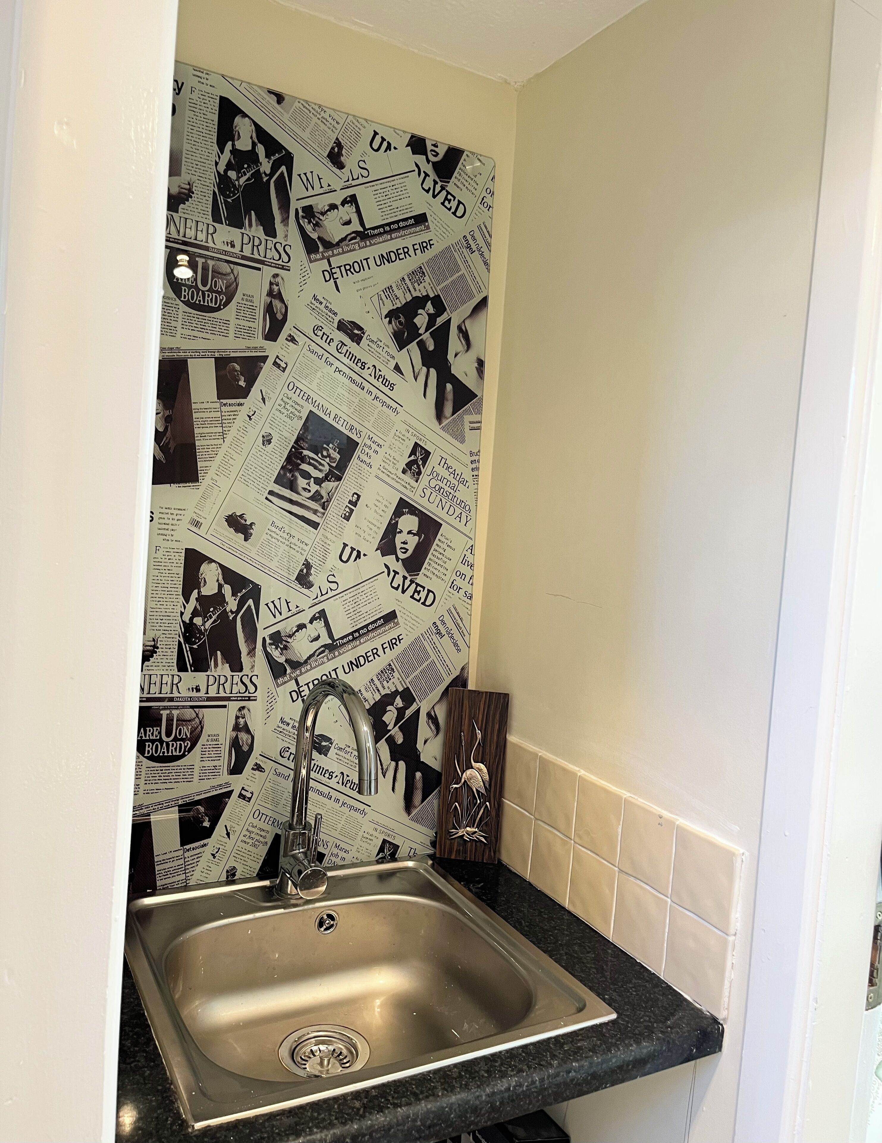 A kitchen with a stainless steel sink, a black countertop, and a wall decorated with newspaper clippings.