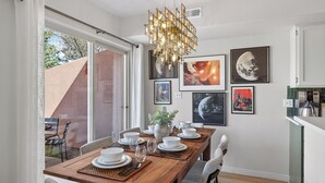 En matplats med ett träbord för fyra personer, en kristallkrona och inramade konstverk på väggen.
